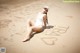 A woman in a white bathing suit sitting on a sandy beach.