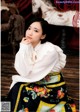 A woman sitting on a wooden floor wearing a white blouse and skirt.