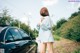 A woman standing next to a black car on a dirt road.