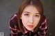 A woman in a red and black plaid shirt leaning against a wall.