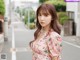 A woman in a pink floral dress standing on a street.