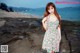 A woman in a floral dress standing on a rocky beach.